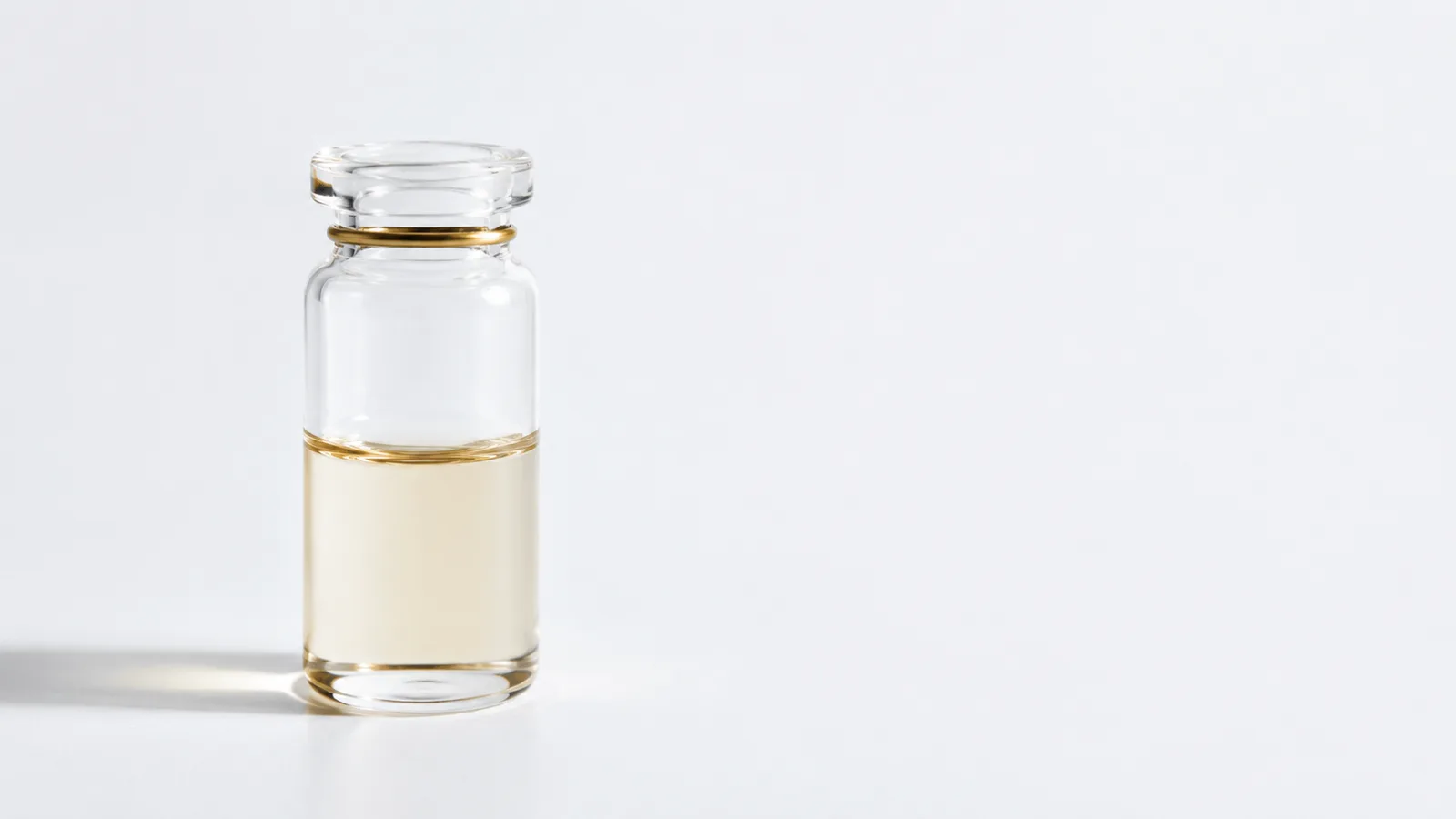 A clear glass vial of pale amber solution on a white surface